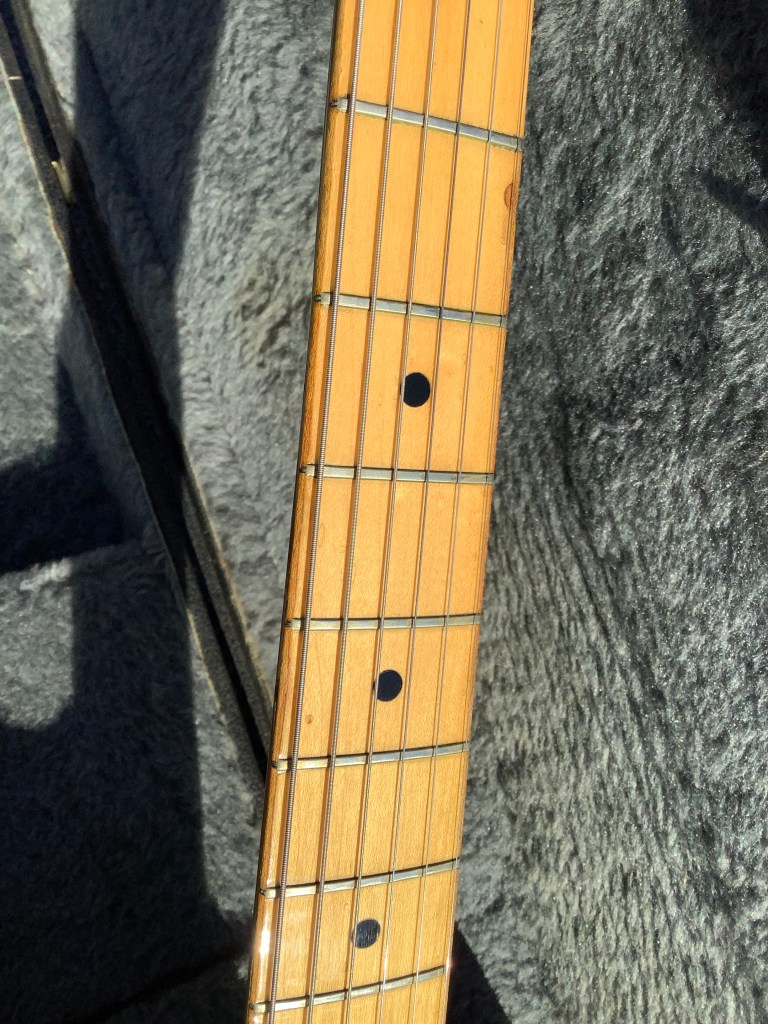 Close-up of the fingerboard of a Fender Telecaster guitar, showcasing the frets and inlay dots, with a soft fabric background.