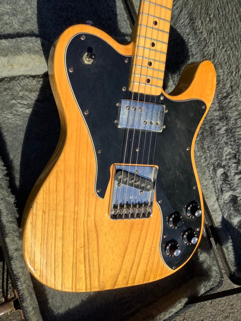 Close-up of a natural wood Fender Telecaster Custom Deluxe guitar, featuring an autographed back by Rick Parfitt and Francis Rossi. The guitar has a custom humbucker in the neck position and a single coil bridge pickup, along with volume and tone controls.