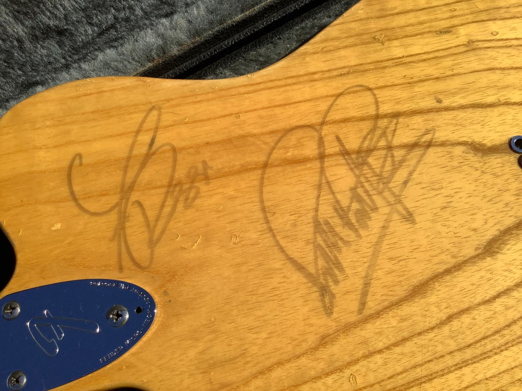 The back of a natural wood Fender Telecaster Custom Deluxe guitar featuring the autographs of two musicians.