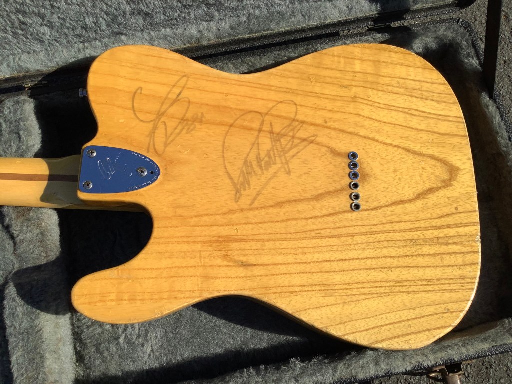 Back view of a natural wood Fender Telecaster Custom Deluxe guitar, featuring autographs from Rick Parfitt and Francis Rossi.