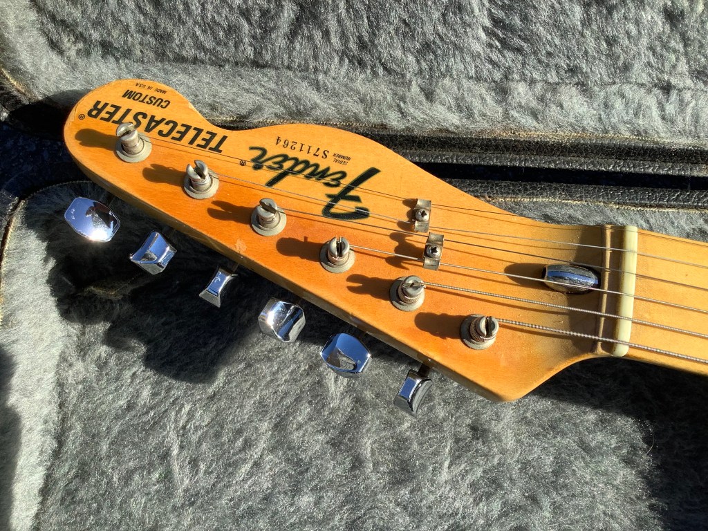 Close-up of the headstock of a Fender Telecaster Custom, featuring tuning pegs and the logo.